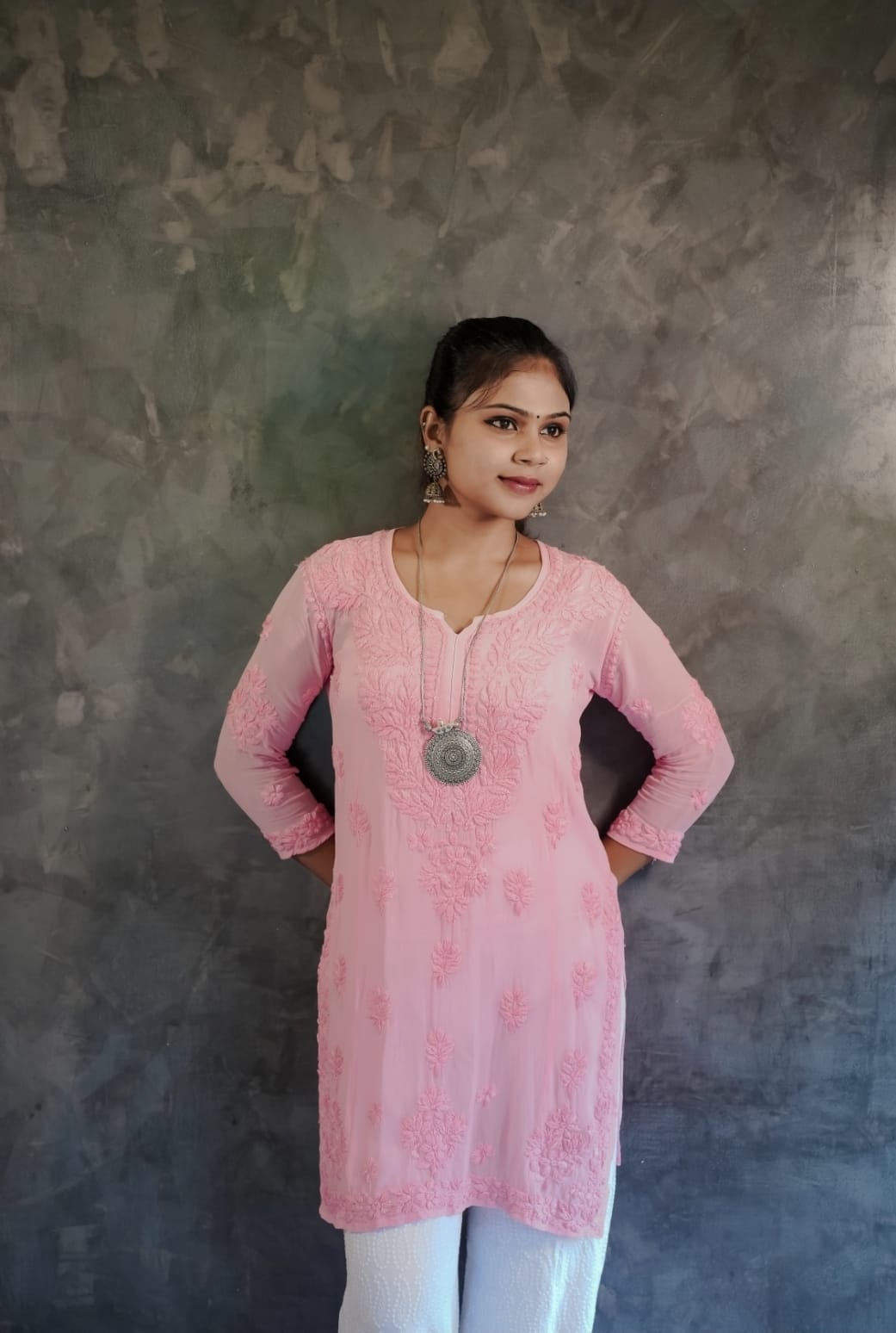 Woman wearing a pink embroidered kurta against a gray background